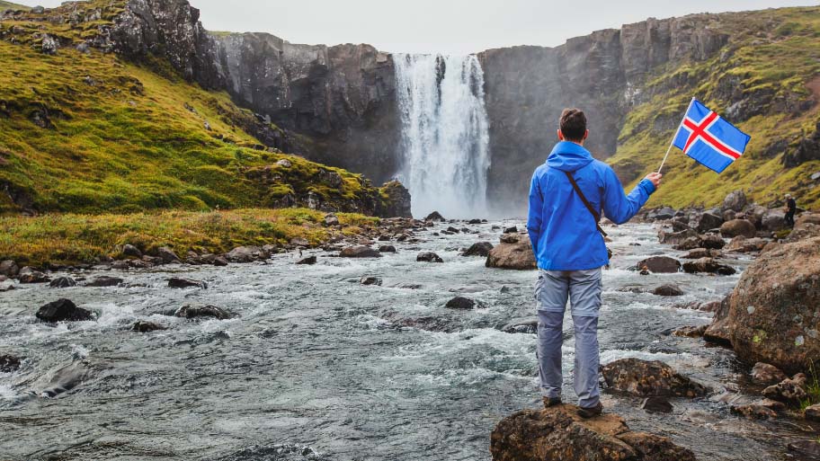 travel to Iceland, tourist holding icelandic flag near scenic waterfall